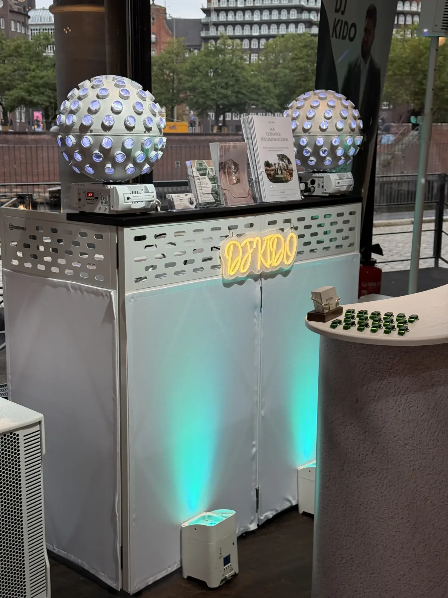 DJ-Booth mit Neon-Schriftzug DJ KIDO, Kugel-Lichteffekten und türkisfarbenen Uplights am Messestand