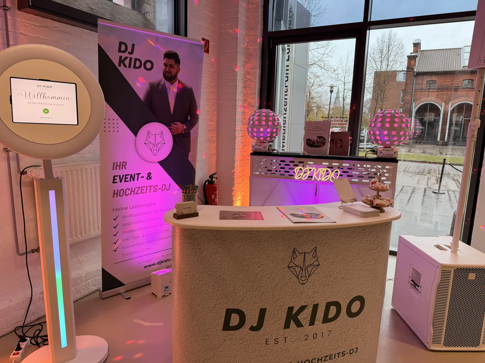 Messestand von DJ Kido auf der Kieler Hochzeitsmesse im Alten Güterbahnhof: Theke, Roll-up, Fotobox, DJ-Booth und Kugel-Lichteffekte vor den Industriefenstern
