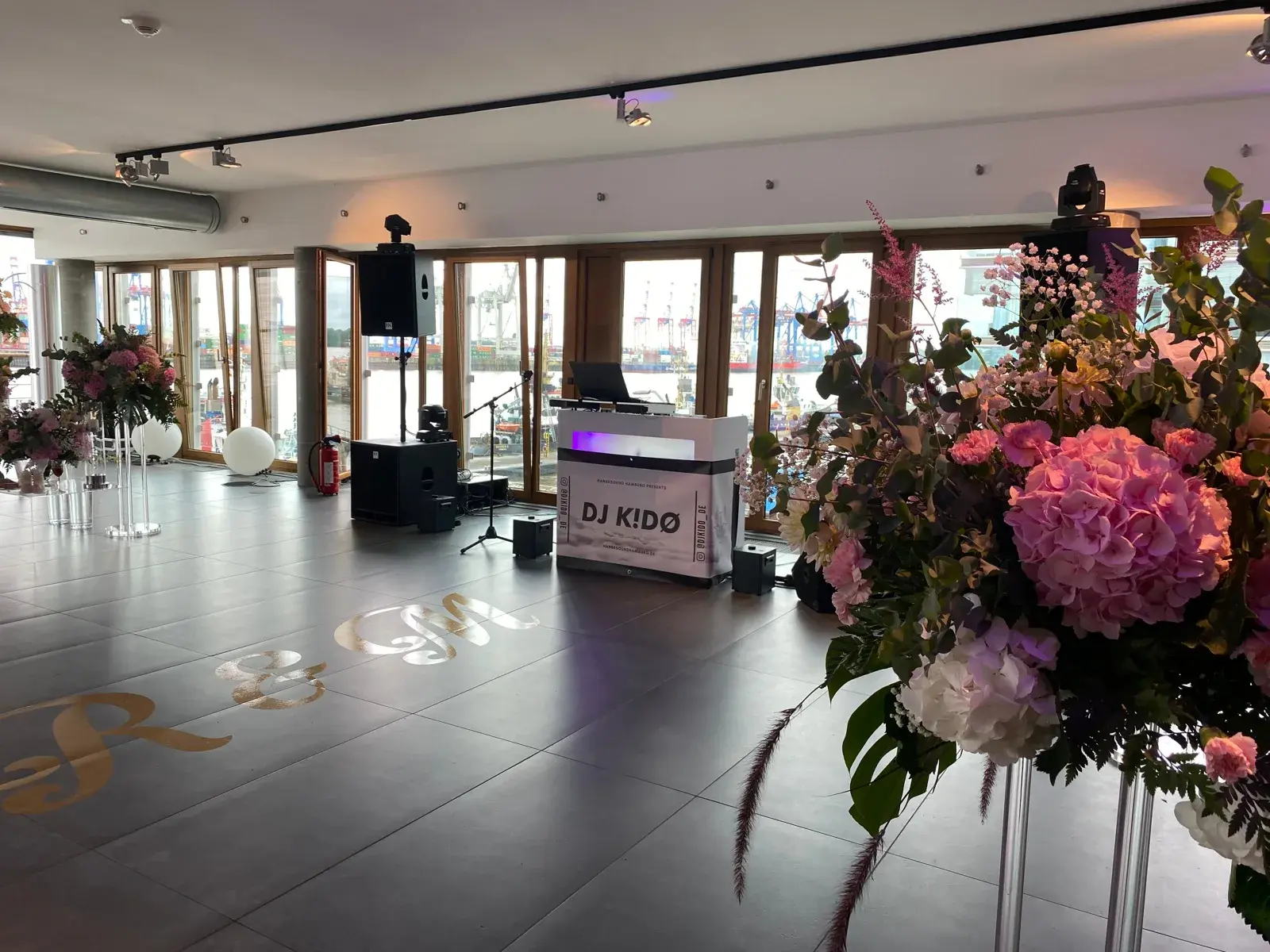 DJ-Pult von DJ Kido vor der Glasfront des view eleven mit Blick auf die Containerbrücken im Hamburger Hafen, davor die Tanzfläche mit den Initialen des Brautpaars