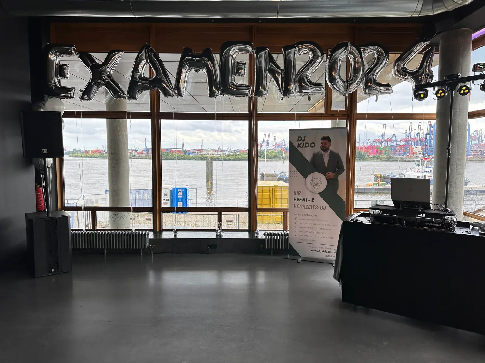DJ-KIDO-Setup bei einer Abschlussfeier im view eleven vor der Glasfront zum Hamburger Hafen und Ballons mit der Aufschrift EXAMEN 2024