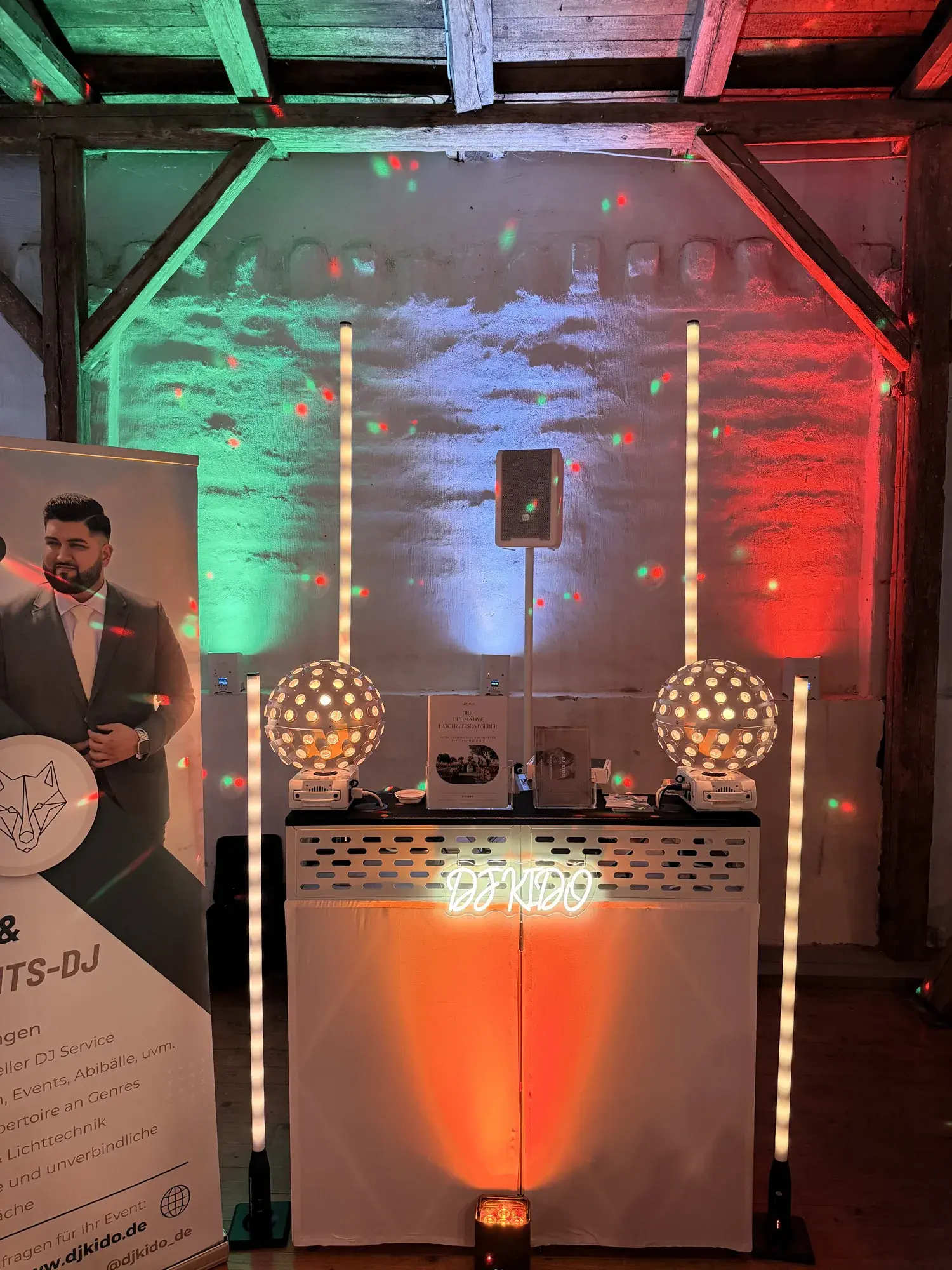DJ-Booth mit Neon-Schriftzug und Lichtsäulen vor der Fachwerkwand der Scheune auf Gut Pronstorf, grün und rot beleuchtet