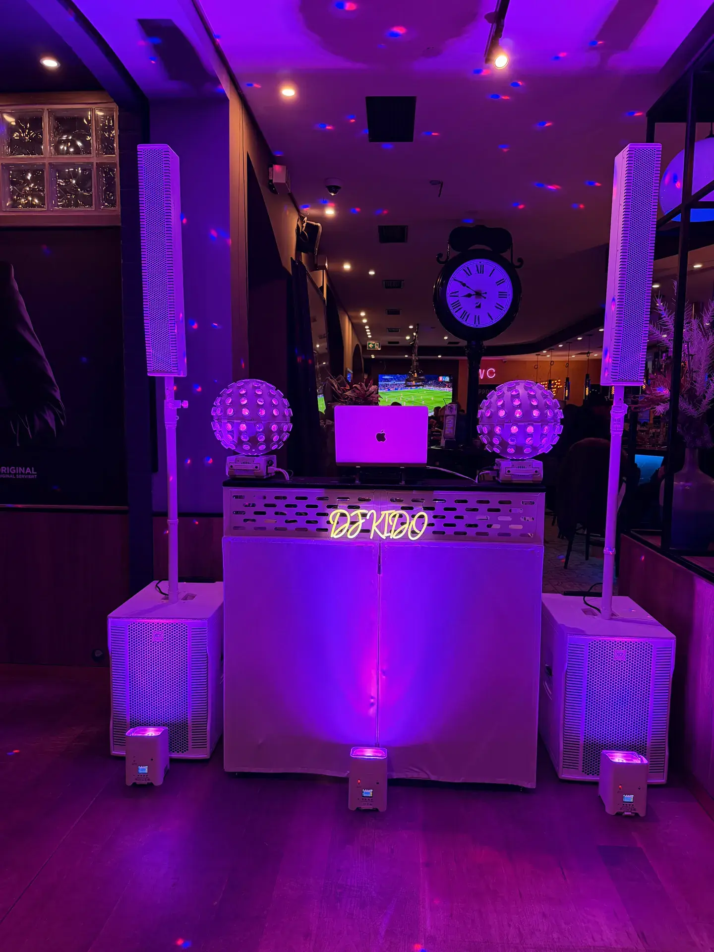 Beleuchtetes DJ-Kido-Setup mit weißer DJ-Booth, Säulenlautsprechern, Subwoofern und kugelförmigen Lichteffekten